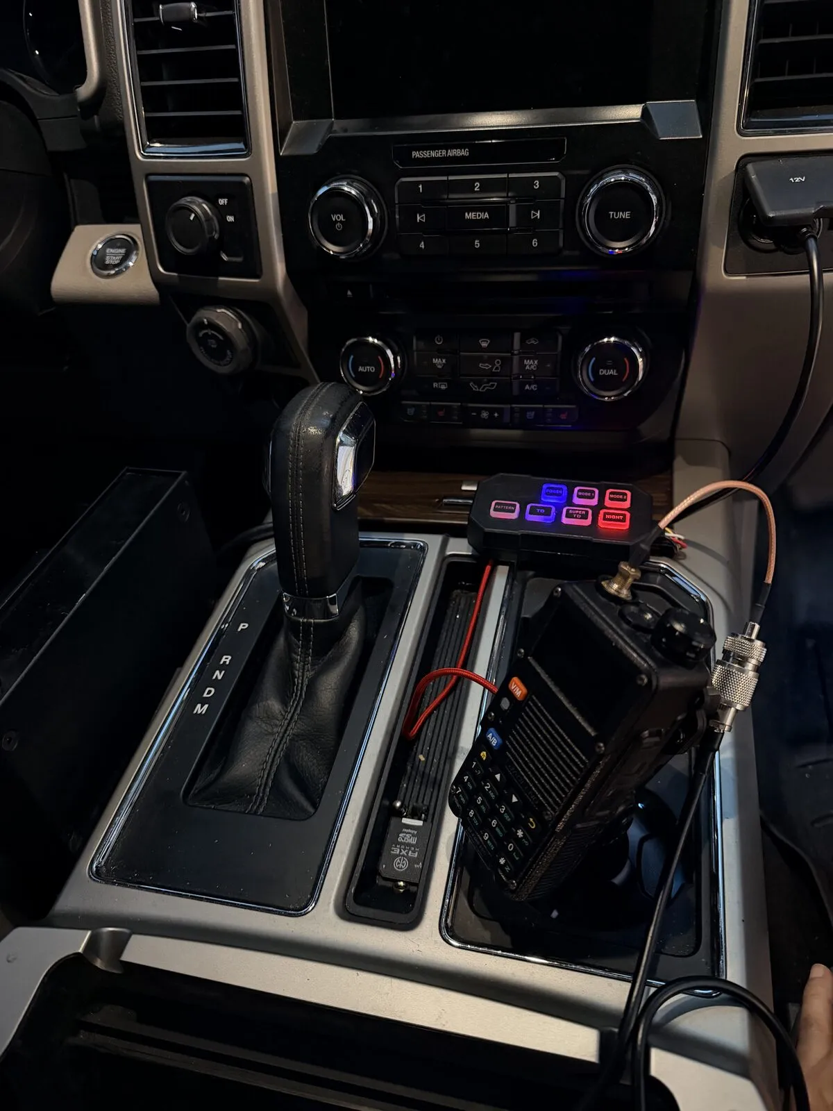 The front console tray ahead of the shifter, with a small switch panel and a handheld radio sitting in it.