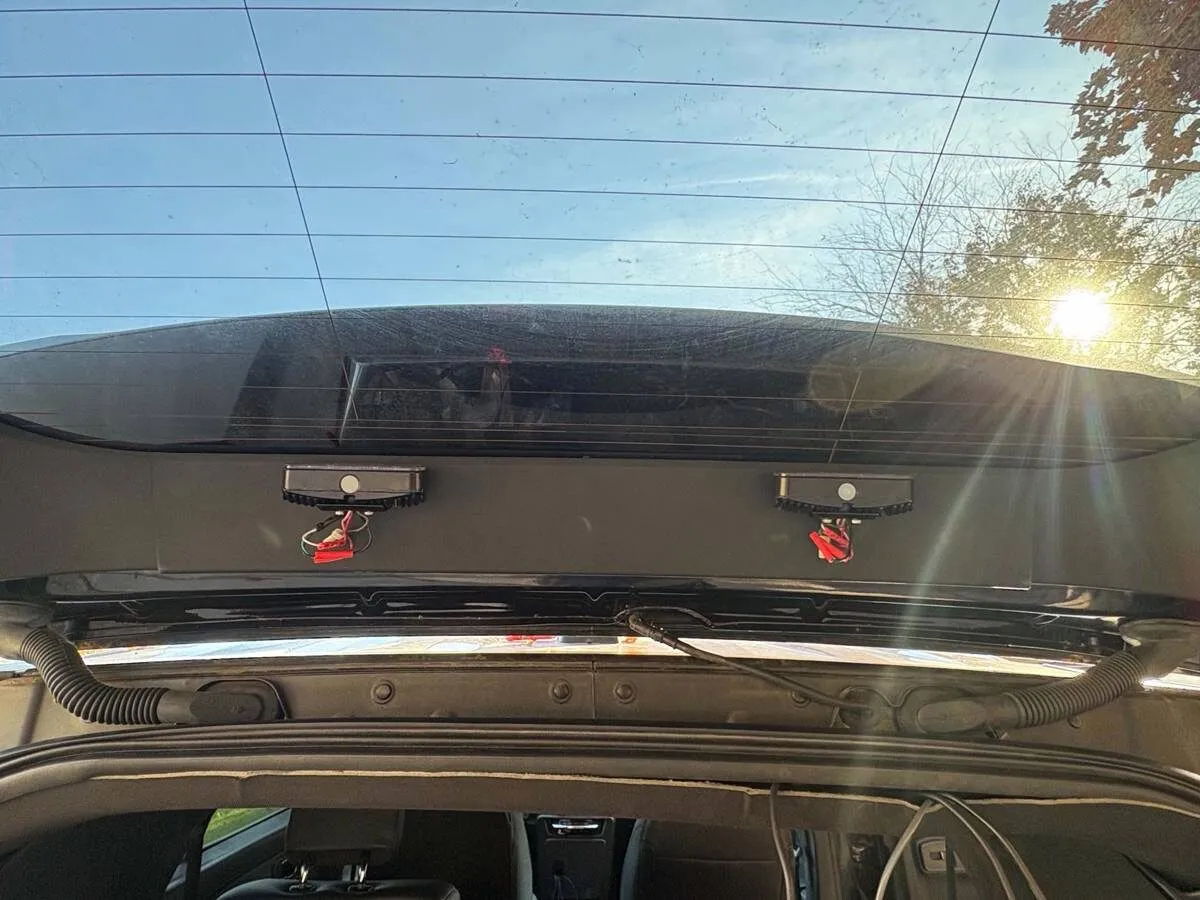 Looking up at the open liftgate from inside, with two small LED warning heads mounted under the rear glass and their leads hanging down.