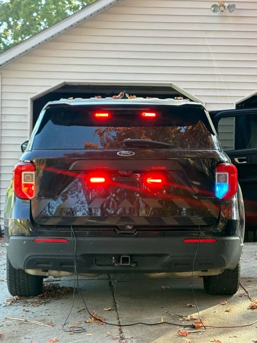 Rear of the demo SUV in a driveway with red warning lights glowing in the rear window and liftgate, and a blue flash in the right taillight.